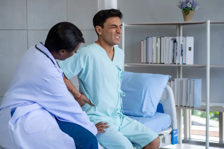 A doctor examines a patient sitting on a hospital bed, grimacing in pain.
