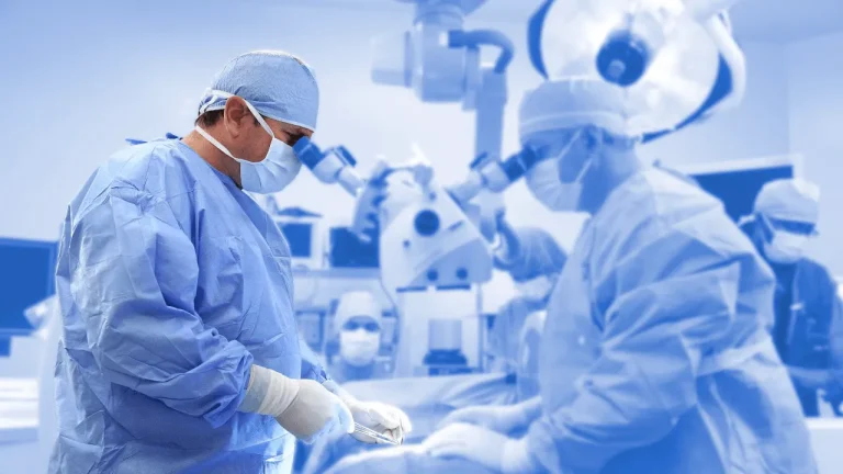 Surgeons in blue scrubs operate in a sterile, well-lit operating room.