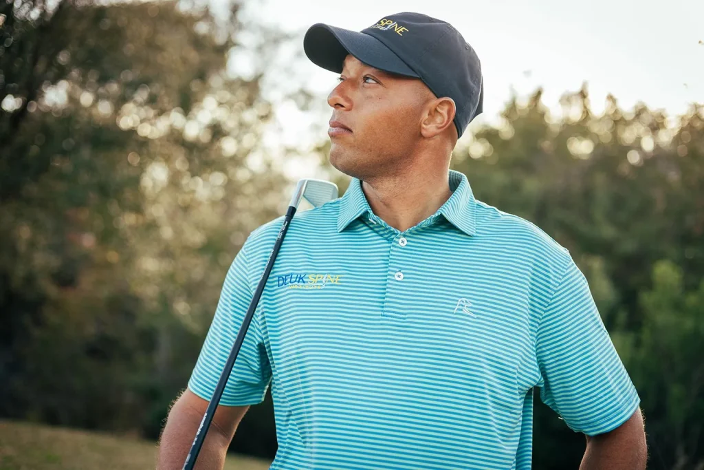 A man in a striped polo shirt and cap holds a golf club outdoors.
