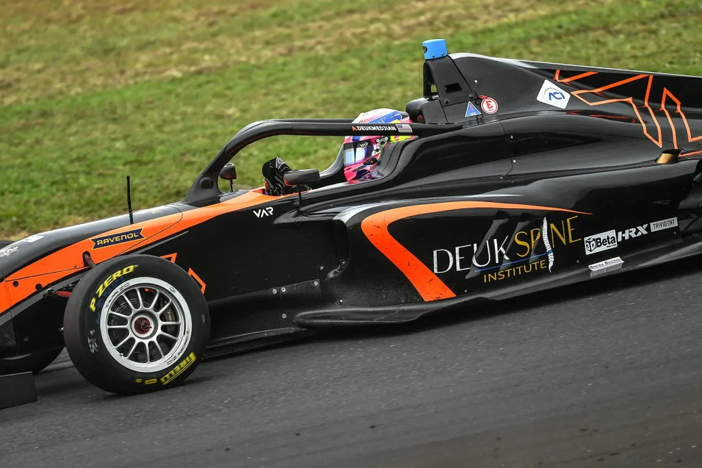 A race car with orange and black livery drives on a track.