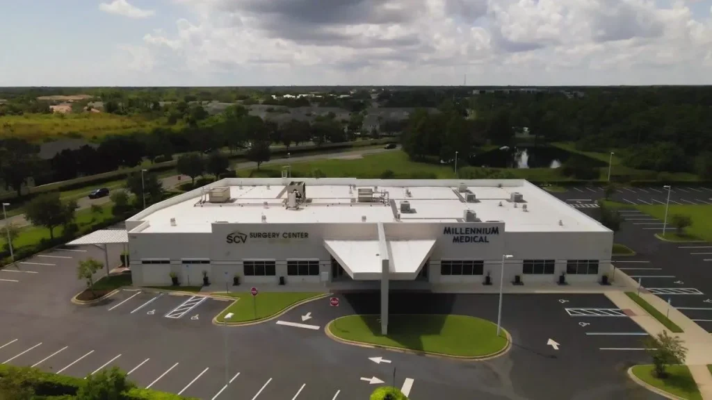Aerial view of a large medical facility with parking lot, surrounded by greenery.