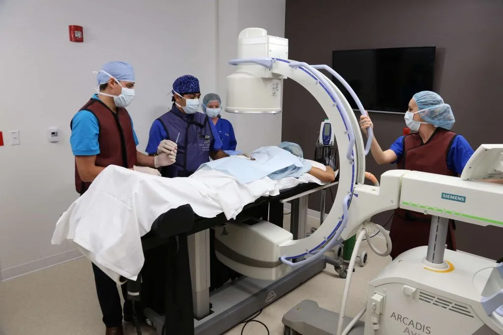 Medical staff in scrubs and protective gear prepare a patient under an X-ray machine.