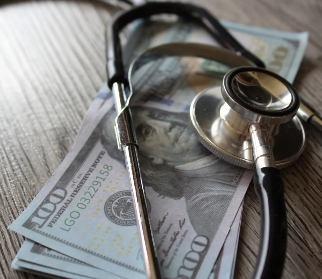 A stethoscope rests on a stack of hundred-dollar bills.