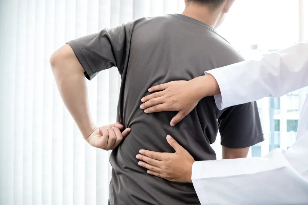 A person holds their back while a doctor examines them.