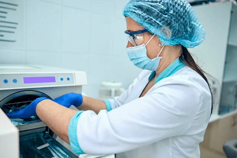 Technician in protective gear operates sterilization equipment.