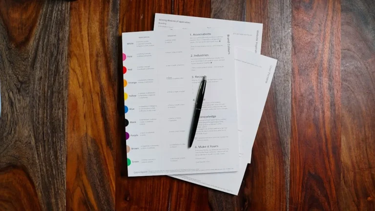A pen rests on top of colorful worksheets on a wooden table.