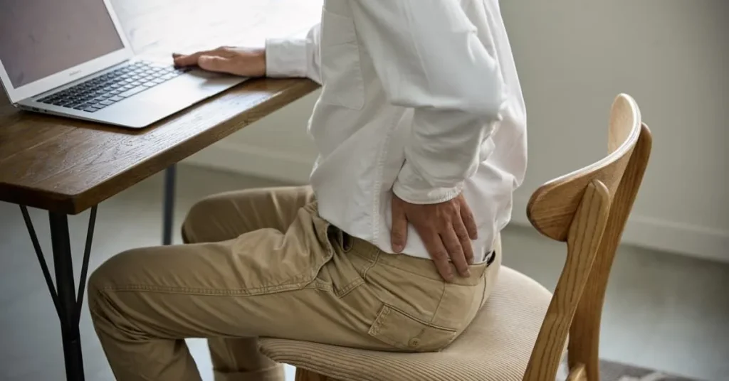 Person sitting at a desk with a laptop, holding their lower back in discomfort.