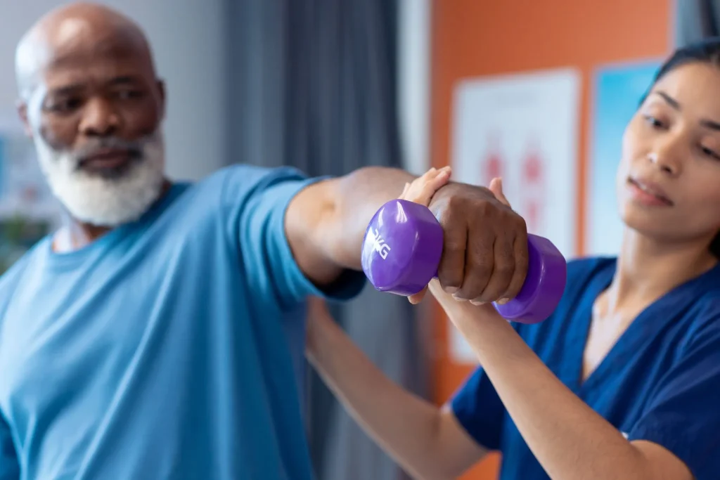 A woman assists a man holding a purple dumbbell during an exercise session.