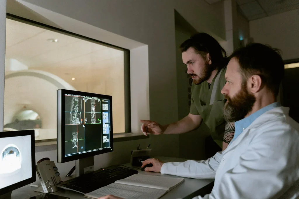 Two doctors analyzing MRI scans on computer screens in a dimly lit room.