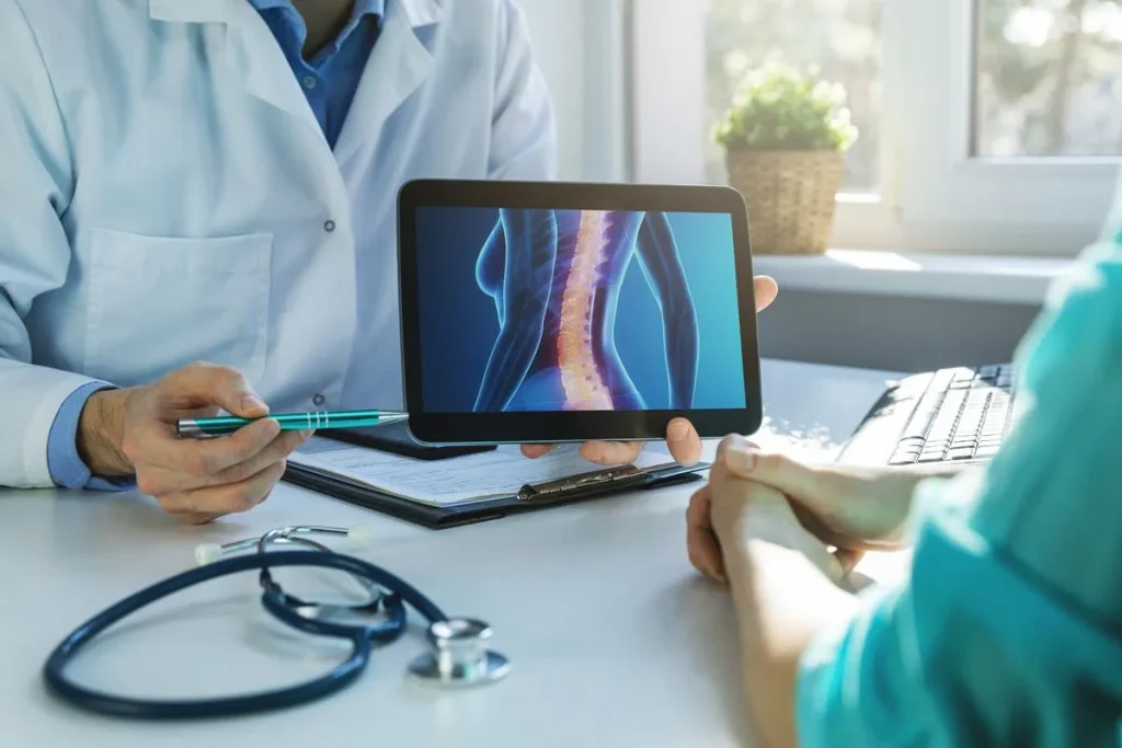 A doctor shows a patient a spinal diagram on a tablet during a consultation.