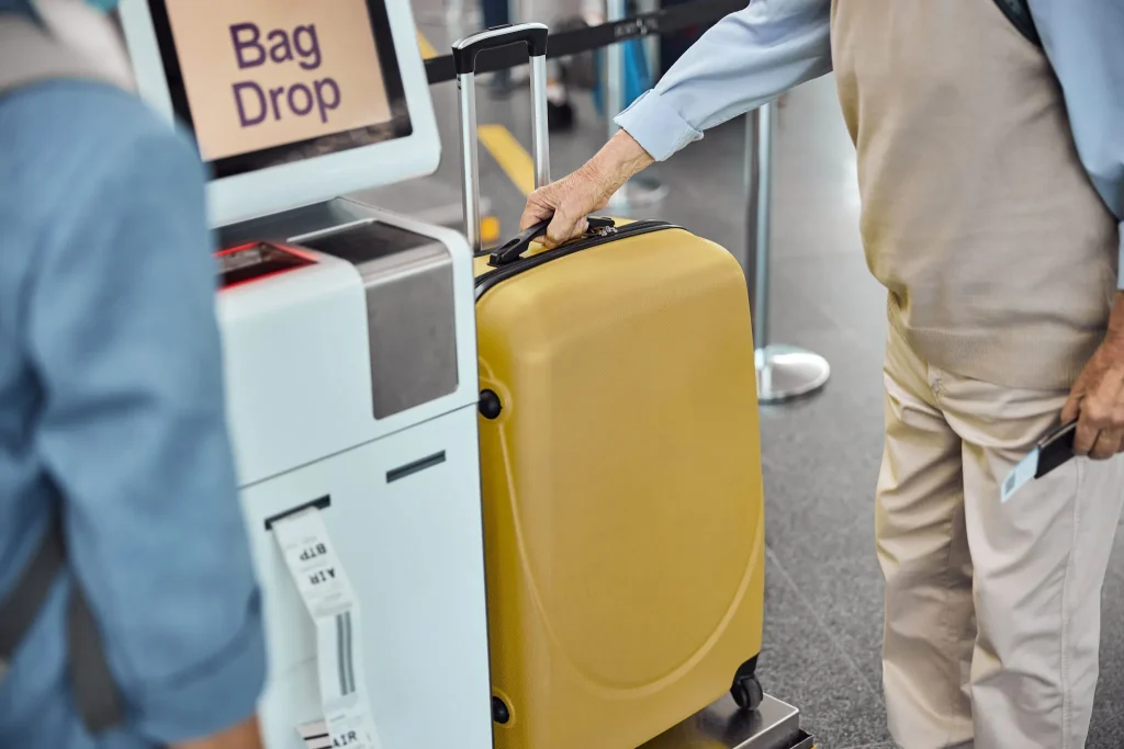 Person placing a yellow suitcase on an airport bag drop scale.