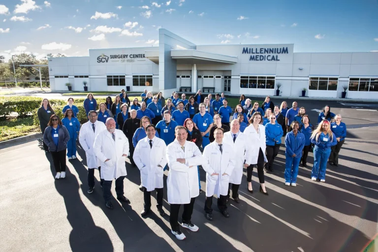 A large group of medical staff stands outside Millennium Medical, wearing white coats and blue uniforms.