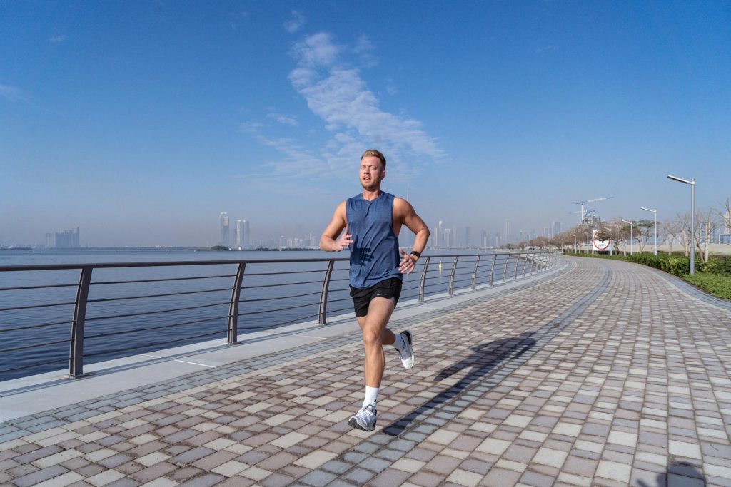 Man running along a waterfront promenade with city skyline in the background.