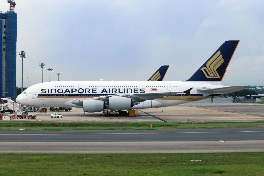 A Singapore Airlines plane parked on the tarmac near an airport runway.