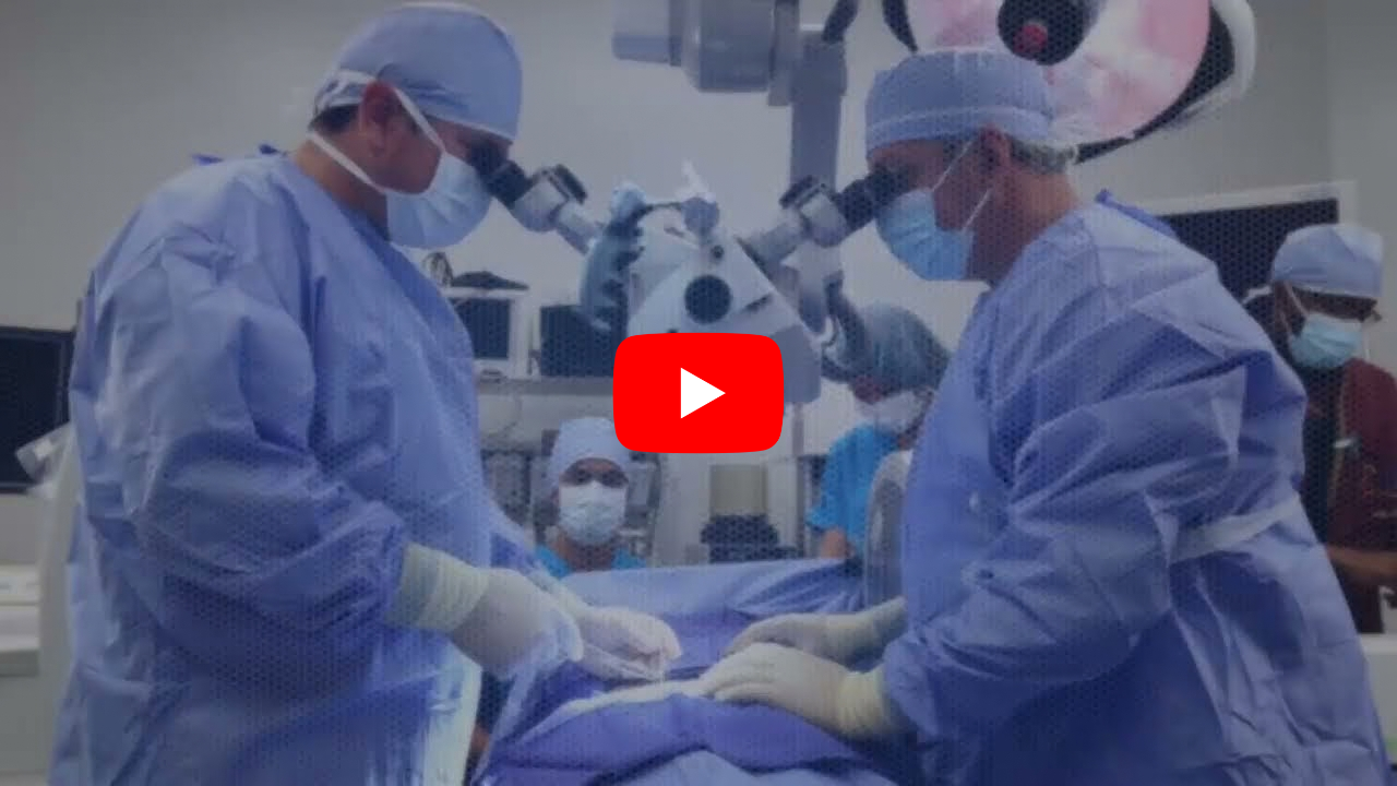 Surgeons in blue gowns and masks perform surgery under a microscope in an operating room.