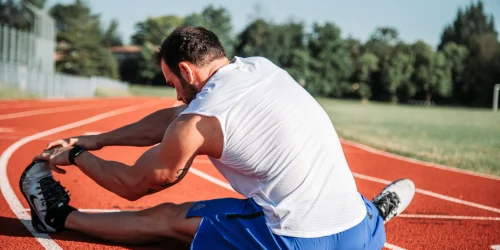 Man stretching on a red running track outdoors.