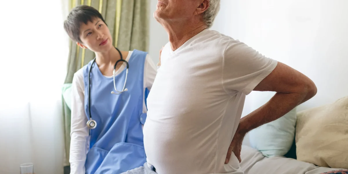 A nurse assists an elderly man experiencing back pain, highlighting the role of nurses in spine surgery and recovery care.
