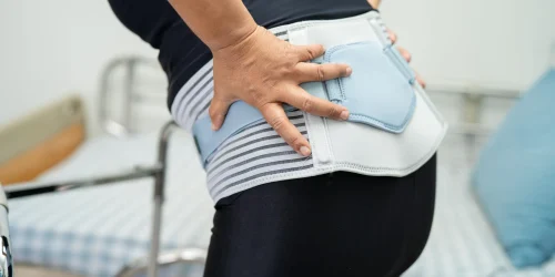 Person wearing a lumbar support brace, holding their lower back.