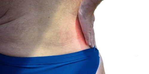 A person holds their lower back, indicating pain from a herniated disc.