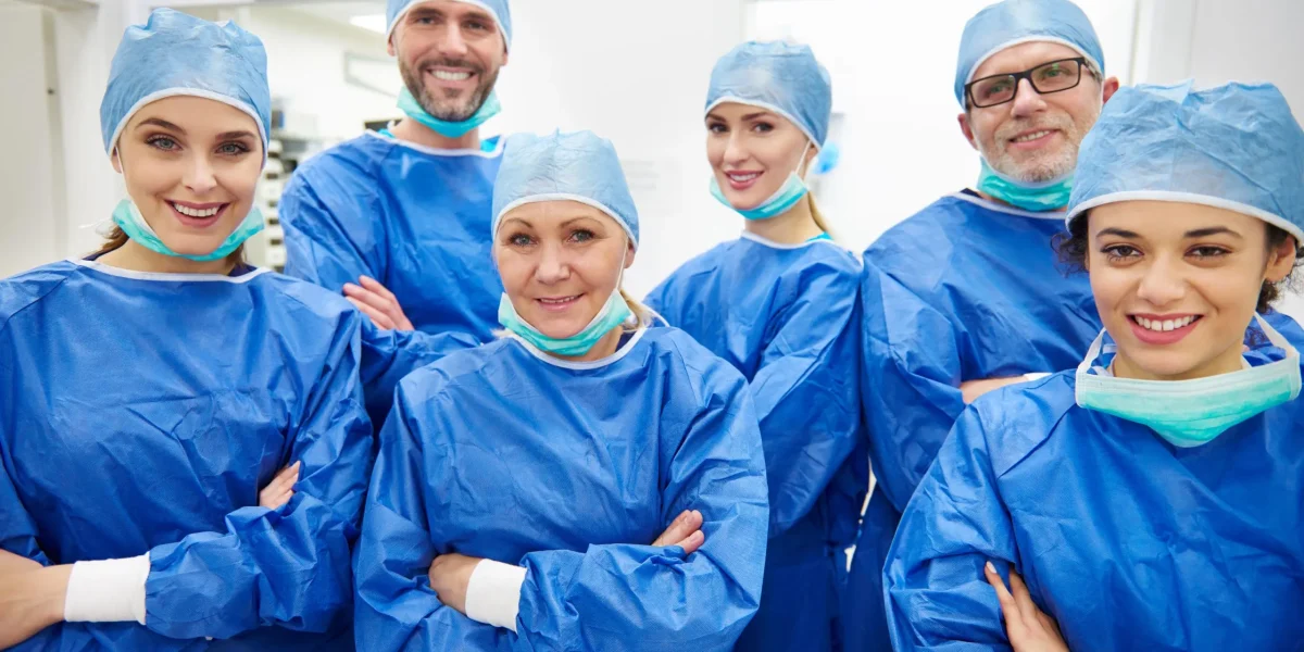 Group of six smiling spine neurosurgeons in blue scrubs and surgical caps.