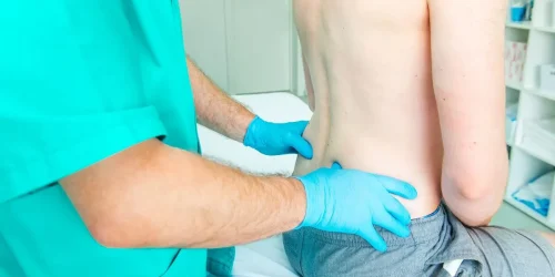 Patient sitting on table having his back examined by a doctor.