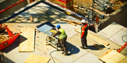 Two construction workers using a table saw at a busy construction site