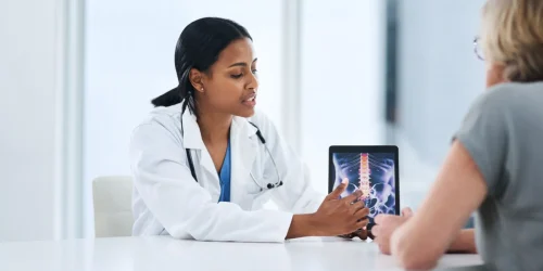 Doctor showing a patient spine X-ray on a tablet during a consultation.
