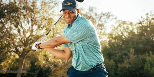 Golfer in mid-swing with a hat, surrounded by sunlight and trees in the background.
