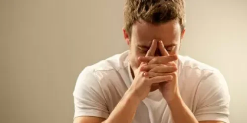Man in white shirt looking stressed with hands covering face.
