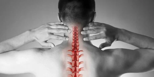 Man with hands on neck, highlighting a red spine illustration on his back.