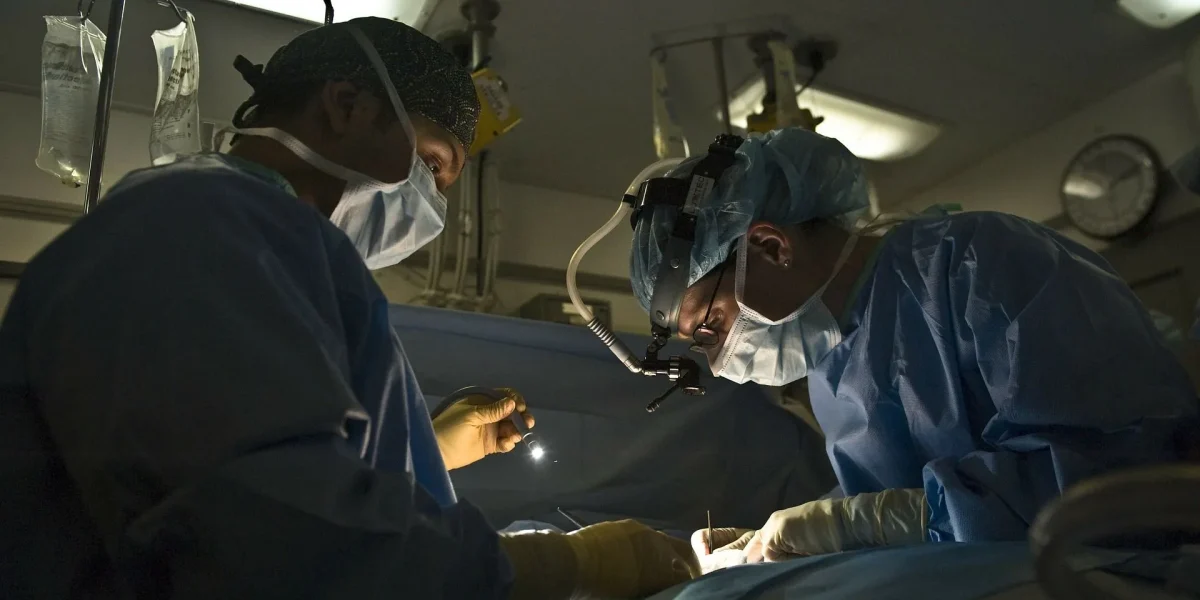 Two surgeons focus intently during a surgical procedure in a dimly lit operating room.