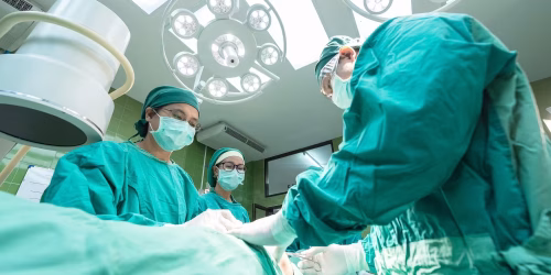 Surgeons in an operating room performing a procedure under bright lights.