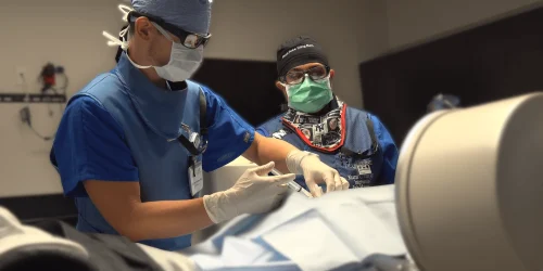 Two surgeons in scrubs and masks perform a procedure in an operating room.