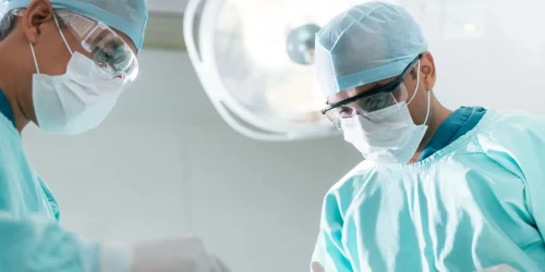 Two surgeons in scrubs and masks operating in a surgical room.