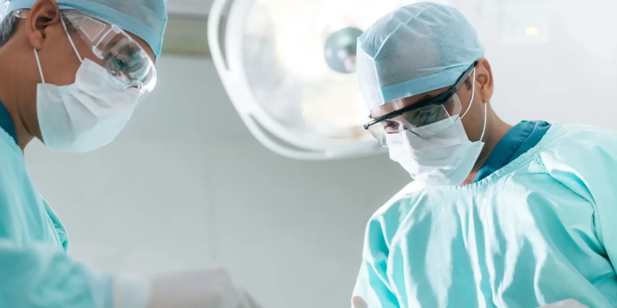 Two surgeons in scrubs and masks operating in a surgical room.