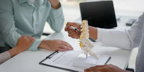 A doctor explains a spine model to a concerned worker regarding compensation paperwork.